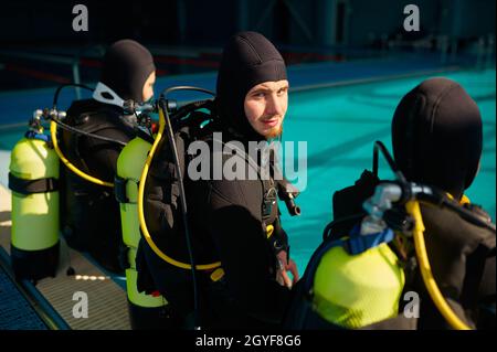 Divemaster et deux plongeurs en équipement de plongée se préparant à l'école de plongée. Apprendre aux gens à nager sous l'eau, piscine intérieure intérieure sur la ba Banque D'Images