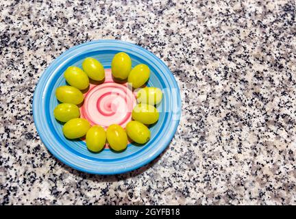 Une assiette bleue décorée d'une spirale rose sur une table en marbre, avec les douze raisins chanceux préparés pour célébrer le nouvel an à la Saint-Sylvestre Banque D'Images