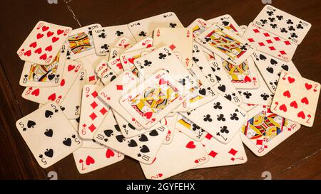 jeu de cartes à jouer comme le poker ou le rummy, éparpillées au hasard sur une table de jeu en bois brun foncé. Banque D'Images