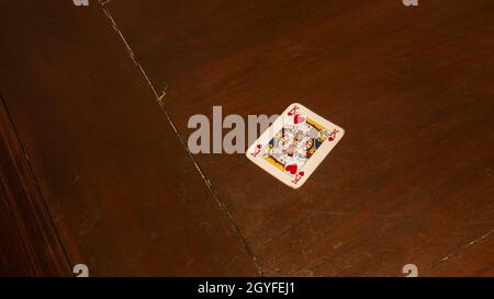 jouer des cartes comme le poker ou le rummy, roi rouge des coeurs, seul sur une table de jeu en bois brun foncé. Banque D'Images