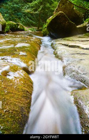 Courant d'eau blanche d'un ruisseau qui coule sur des roches et passe entre de grands blocs dans une forêt Banque D'Images