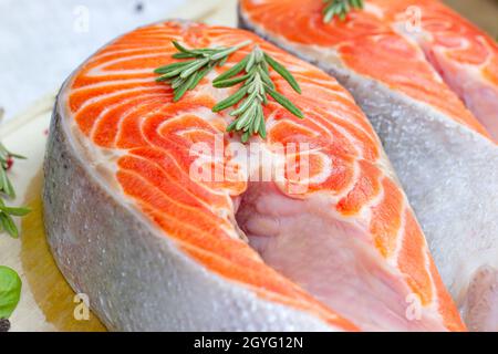 Des tranches de saumon rouge crues au romarin dans la cuisine sur fond de bois clair. Banque D'Images