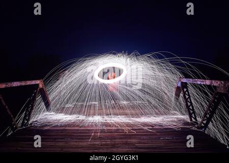 Étincelles blanches avec un anneau de lumière autour d'un homme sur un pont la nuit Banque D'Images