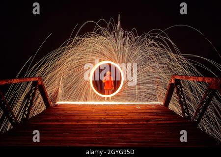 Homme sur un pont avec un cercle de lumière et d'étincelles la nuit Banque D'Images