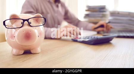 Bannière avec une banque de porc portant des lunettes sur la table du comptable qui travaille en arrière-plan Banque D'Images