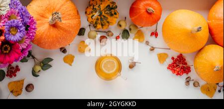 Aménagement d'automne avec une tasse de thé au citron, citrouilles, feuilles jaunes séchées, bouquet de fleurs d'automne, baies roses guelder,glands, et châtaignes sur bac blanc Banque D'Images