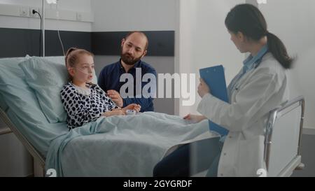 Médecin médecin médecin médecin discutant du traitement de la maladie avec un enfant malade et un père au cours d'un examen médical en salle d'hôpital. Enfant hospitalisé se reposant dans le lit se rétablissant après une chirurgie respiratoire Banque D'Images