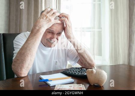 beau homme aux cheveux gris de 88 ans dans le concept de planification budgétaire, un vieil homme, s'assied à la maison et compte l'argent, écrit les dépenses. Banque D'Images