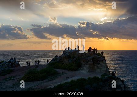 LIBAN, BEYROUTH, RAS BEYROUTH, TOURISTES ET LIBANAIS SUR UN ROCHER AU BORD DE LA MER AU COUCHER DU SOLEIL PRÈS DE PIGEON ROCK (RAOUCHE) Banque D'Images