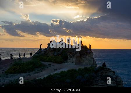 LIBAN, BEYROUTH, RAS BEYROUTH, TOURISTES ET LIBANAIS SUR UN ROCHER AU BORD DE LA MER AU COUCHER DU SOLEIL PRÈS DE PIGEON ROCK (RAOUCHE) Banque D'Images