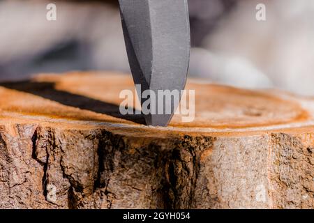 La lame aiguisée d'un couteau est coincée dans une souche en bois et crée une ombre. Banque D'Images