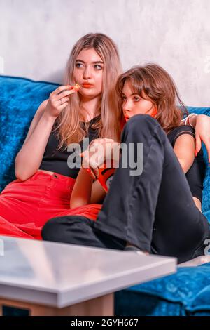 Une jeune fille adolescente regarde la télévision avec sa mère pendant qu'elle se câlin sur un canapé tout en s'accrotant au pop-corn dans une grande baignoire dans une pièce mal éclairée Banque D'Images