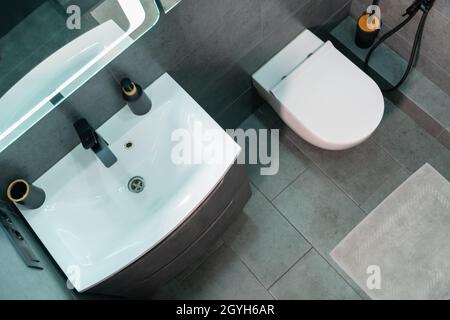 Vue en hauteur d'un intérieur moderne monochrome de salle de bains avec meuble-lavabo blanc simple et toilettes murales sur sol carrelé gris avec tapis de bain Banque D'Images