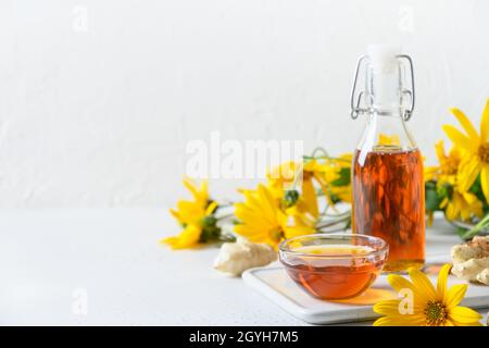 Sirop d'artichaut topinambour en bouteille, fleurs et racine sur fond blanc.Copier l'espace. Banque D'Images