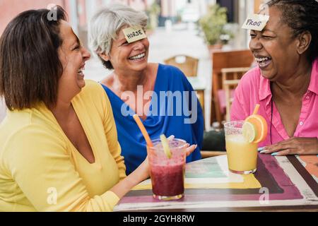 Multiracial senior femmes ayant le plaisir de jouer à deviner jeu de front au bar restaurant - Focus sur le visage de femme africaine Banque D'Images