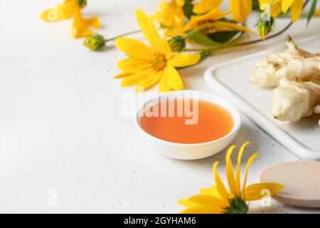 Sirop d'artichaut Jérusalem dans un bol, fleurs et racine sur fond blanc.Gros plan.Copier l'espace. Banque D'Images