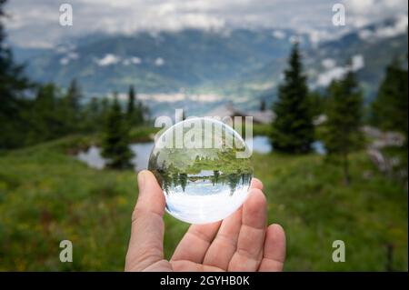 Main tenant la sphère de verre devant le pâturage, jour nuageux en été, alpes dans le Tyrol oriental (Autriche) Banque D'Images