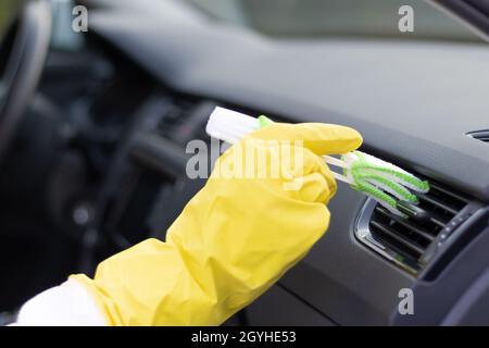 Une main dans des gants en caoutchouc jaune essuie le tableau de bord d'une voiture de la poussière avec une brosse spéciale lors d'un jour d'automne brillant.Mise au point sélective.Gros plan Banque D'Images