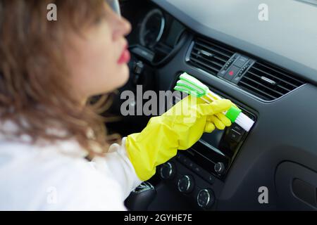 Une fille en gants de caoutchouc jaune essuie le tableau de bord d'une voiture de la poussière avec une brosse spéciale lors d'un jour d'automne brillant.Mise au point sélective.Gros plan Banque D'Images