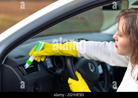 Une fille en gants de caoutchouc jaune essuie le tableau de bord d'une voiture de la poussière avec une brosse spéciale lors d'un jour d'automne brillant.Mise au point sélective.Gros plan Banque D'Images