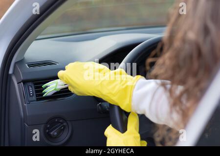 Une fille en gants de caoutchouc jaune essuie le tableau de bord d'une voiture de la poussière avec une brosse spéciale lors d'un jour d'automne brillant.Mise au point sélective.Gros plan Banque D'Images