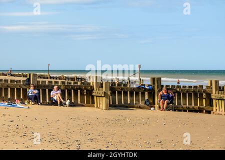 Les gens se détendent et bronzer avec leur dos à une groyne en bois lors d'une journée de septembre glorieuse sur la plage de Mundesley, Norfolk, Angleterre. Banque D'Images