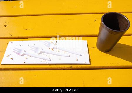 Trois fourchettes en plastique sur un morceau de carton avec chapelure et une tasse de café vide sur une table en bois jaune. Banque D'Images