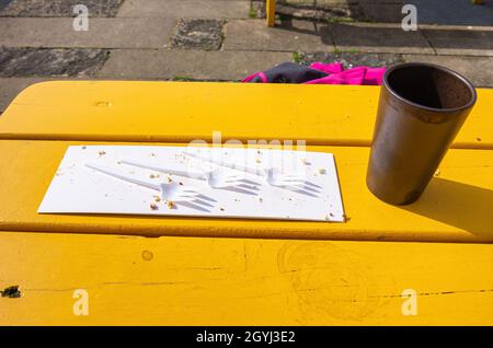 Trois fourchettes en plastique sur un morceau de carton avec chapelure et une tasse de café vide sur une table en bois jaune. Banque D'Images