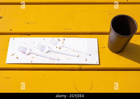 Trois fourchettes en plastique sur un morceau de carton avec chapelure et une tasse de café vide sur une table en bois jaune. Banque D'Images