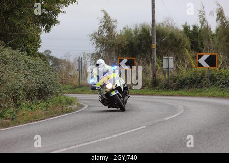 Une moto de police dans un virage sur une route de campagne dans l'Essex. L'officier fait partie d'une équipe qui déblayage la route avant une course à vélo. 'Course de cycle d'arrêt'. Banque D'Images