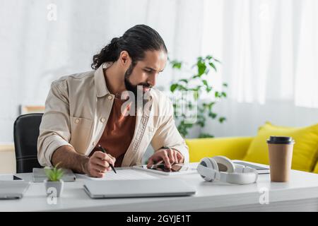 freelance latine barbu utilisant une tablette numérique tout en travaillant avec des documents à la maison Banque D'Images