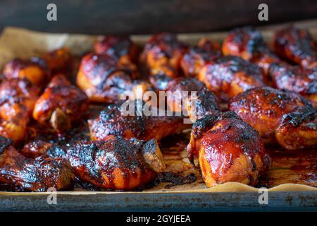 Bâtonnets de poulet cuits au four marinés au barbecue et au miel, chauds et frais sur une plaque de cuisson.Gros plan avec arrière-plan flou. Banque D'Images