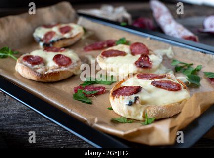 Sandwichs cuits au four à base de muffin anglais et recouverts de cheddar irlandais et de salami espagnol serrano. Banque D'Images