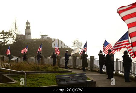 Les membres des Patriot Riders et de la Légion américaine affichent des drapeaux américains et l'enseigne de la Garde côtière tandis que les membres de la Station de la Garde côtière Cape déception organisent un hommage de 21 armes à feu en arrière-plan près du phare de Cape déception à Ilwaco, Washington, le 11 janvier 2020.Le salut de 21 armes à feu était au nom des gardes-côtes perdus dans l'exercice de leurs fonctions dans le Nord-Ouest du Pacifique.(É.-U.Photo de la Garde côtière par Petty Officer 1er Class Levi Read) Banque D'Images