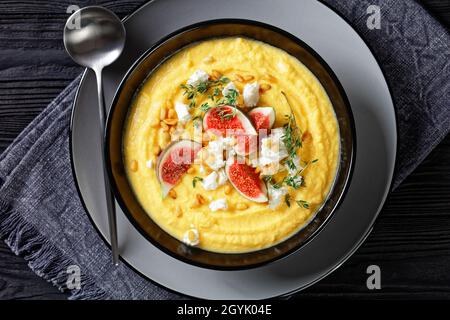 Soupe à la crème de potiron au thym servie dans un bol noir avec féta et figues servies sur un fond en bois avec une cuillère, vue du dessus, gros plan Banque D'Images