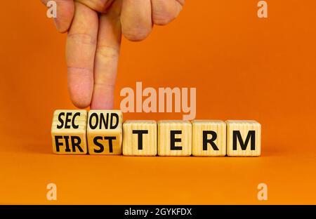 Symbole du premier ou du deuxième terme.L'homme d'affaires tourne des cubes en bois, change les mots du premier terme au deuxième terme.Belle table orange, fond orange.Bus Banque D'Images