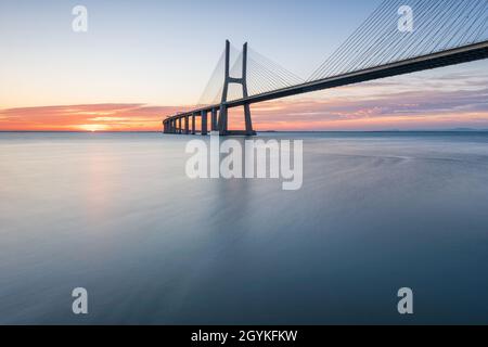 Arrière-plan avec lever de soleil coloré sur le pont de Lisbonne. Le pont Vasco da Gama est un point de repère et l'un des plus longs ponts du monde. réseau local urbain Banque D'Images