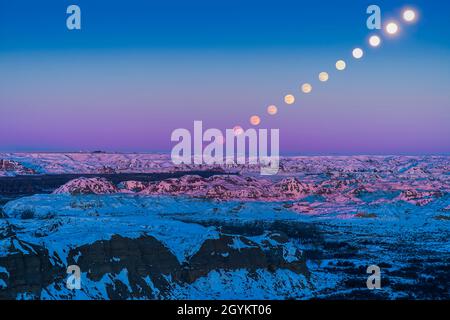 Une image composite de la montée de la pleine lune du 29 décembre 2020 'froide' dans un ciel très clair de nuit crépuscule, ici au-dessus des Badlands de Dinosaur P Banque D'Images