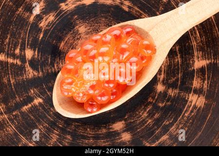 Caviar rouge légèrement salé de saumon kéta avec une cuillère en bois sur un plateau en argile, vue rapprochée du dessus. Banque D'Images