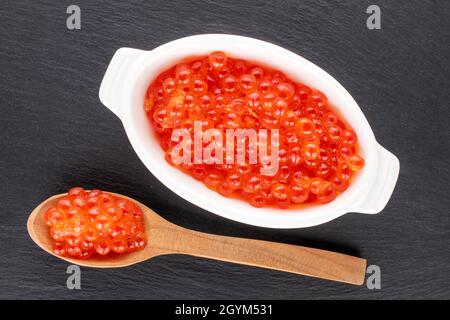 Caviar rouge légèrement salé de saumon kéta avec une cuillère en bois et des plats en céramique blanche sur une pierre d'ardoise, vue rapprochée, vue de dessus. Banque D'Images