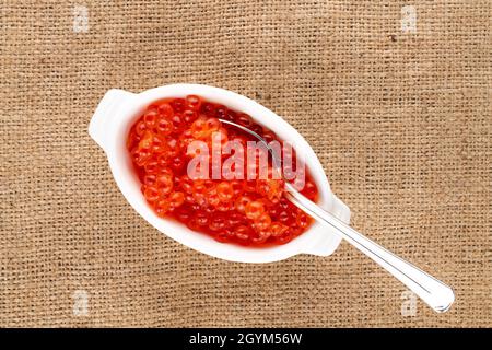 Caviar rouge légèrement salé de saumon kéta avec une cuillère en métal et des plats en céramique blanche sur la viande, vue rapprochée, vue de dessus. Banque D'Images