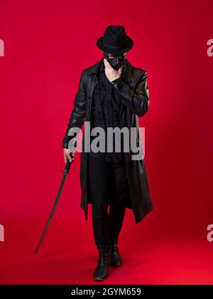 Un mystérieux assassin ninja dans un style noir. Un homme en cuir noir avec un manteau et un chapeau, couvre son visage avec un masque et utilise un katana. Photo Banque D'Images