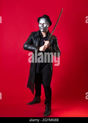 Un mystérieux assassin ninja dans un style noir. Un homme en vêtements noirs avec un cape et un chapeau, couvre son visage avec un masque et utilise un katana. Photo sur rouge Banque D'Images