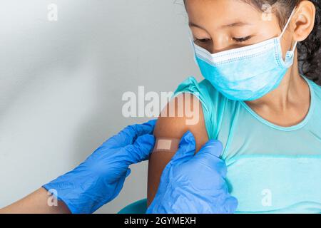 Médecin en gants de protection en caoutchouc bleu mettant un bandage adhésif sur le bras d'une jeune fille après avoir blessé la peau ou injecté le vaccin. Premiers soins. Médical, p. Banque D'Images