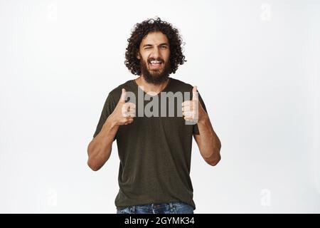 Beau mec souriant se déplaît, montre les pouces dans l'approbation, d'accord et comme, le soutien smth bon, louange grand travail, fond blanc Banque D'Images