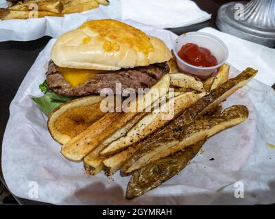 Vue inclinée vers le bas d'un cheeseburger graisseux et de frites au steak croustillantes, servi dans un panier lors d'une plongée de hamburger locale Banque D'Images