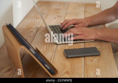 Gros plan des mains d'un homme tapant sur un clavier, à la recherche d'informations. Un rédacteur pigiste travaille sur un projet. Le concept de travail à distance. Photo de haute qualité Banque D'Images