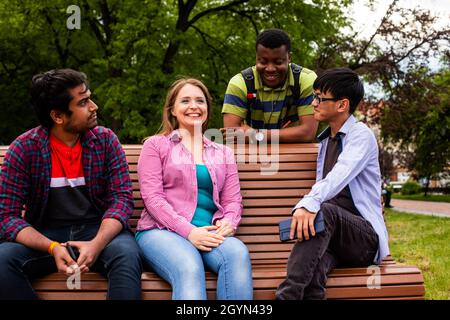 Joyeuse compagnie diversifiée d'amis d'université sur banc en bois Banque D'Images