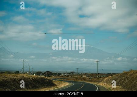 Rencontrez des animaux sauvages comme la Giraffe qui traverse la route d'Oloitoktok et le montKilimanjaro View - Parc national d'Amboseli Banque D'Images