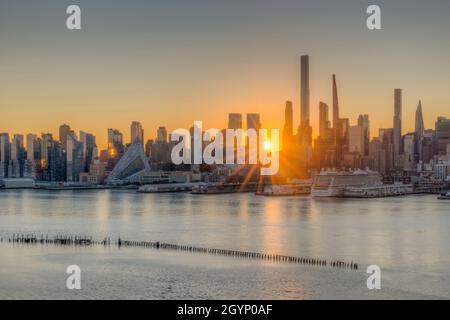 Lever du soleil à New York, à travers des bâtiments dans la ligne d'horizon du côté ouest de Manhattan, vue sur l'Hudson depuis le New Jersey. Banque D'Images